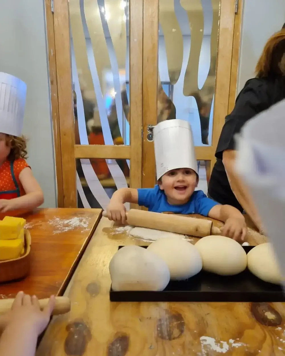 A young chef in a white hat rolling pizza dough at a Dario's pizza party